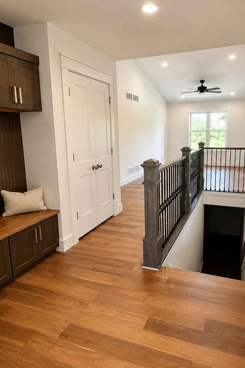 Oak & Origin custom home interior, Wisconsin Entryway with hardwood floors, built-in bench, and open staircase railing.